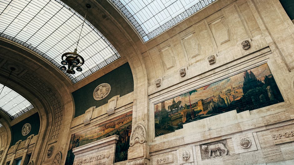 Inside a grand, historic building featuring high arched ceilings and large glass skylights that allow natural light to fill the space. The walls are made of light-colored stone with decorative archite
